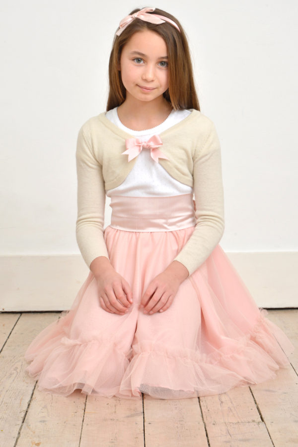 A girl kneeling in a pale pink tulle skirt and an ivory wool d=cardigan with pink bow - The Little Wedding Company