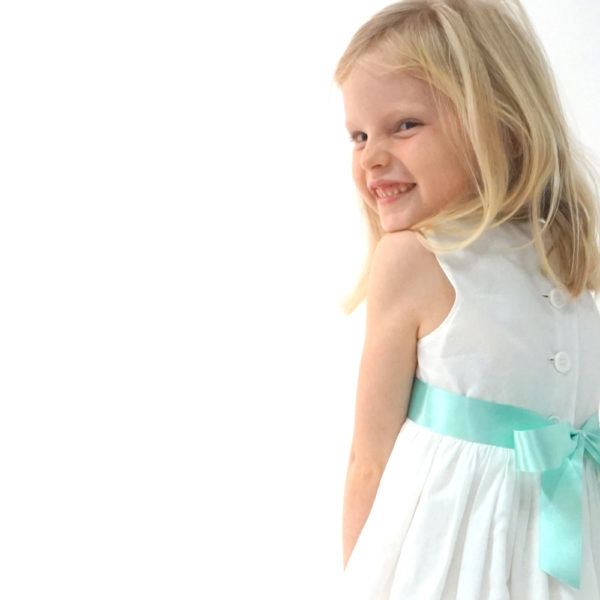 A picture of a flowergirl wearing an ivory cotton dress with an aqua ribbon bow - The Little Wedding Company