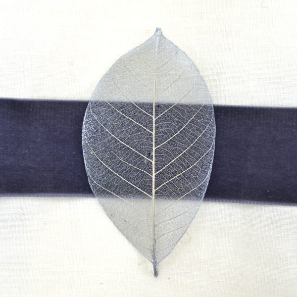 A close up image of a silver skeleton leaf sitting on a charcoal grey velvet ribbon - The Little Wedding Company