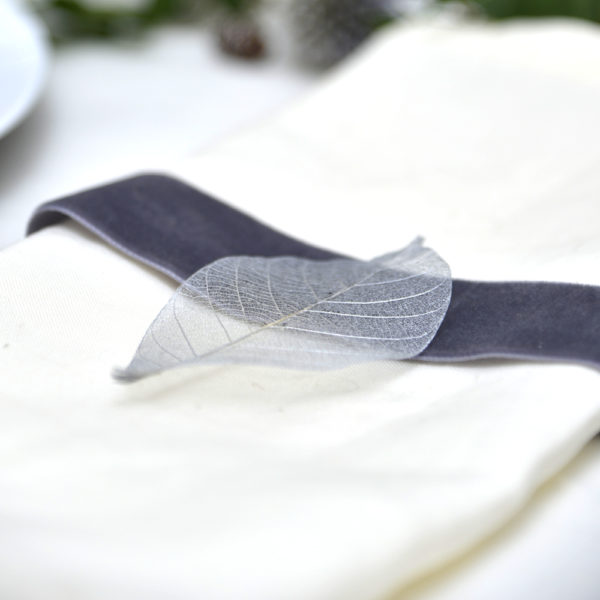 An ivory napkin with a charcoal velvet ribbon and a silver skeleton leaf on it - The Little Wedding Company