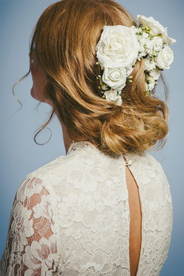 A woman wearing a lace dress with a large rose hairpiece in her hair - The Little Wedding Company
