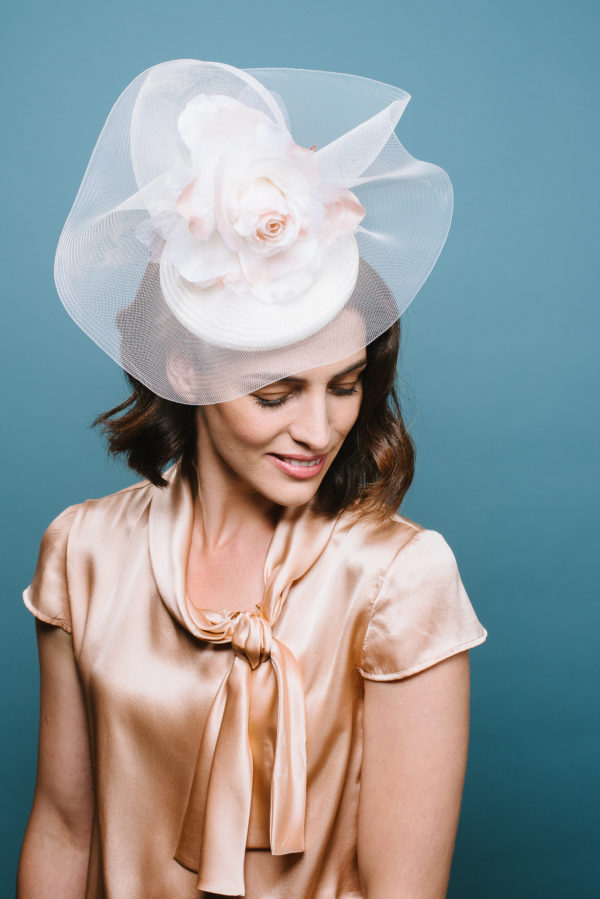 Woman wearing a small white hat with a crinoline swirl and an ivory silk rose on the top - The Little Wedding Company