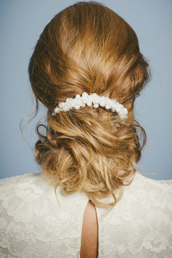 A woman wearing an ivory lace dress and a pearl hairpiece in her hair - The Little Wedding Company