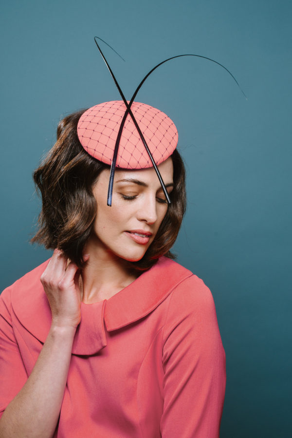 Woman wearing small pink hat with coloured quills and net - The Little Wedding Company