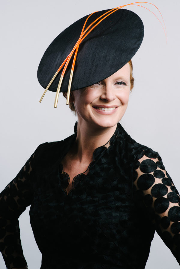 A woman wearing a nave dress with a navy hat with three orange quills - The Little Wedding Company