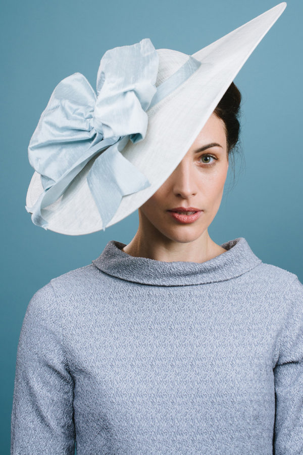 A lady wearing a pale blue boatneck dress with a white hat with pale blue taffeta bow - The Little Wedding Company