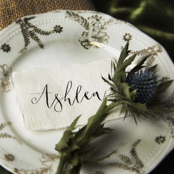 A picture of a plate with a white hand written place name on handmade paper - The Little Wedding Company