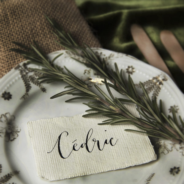 A picture of a plate with a piece of rosemary and a handwritten name place - The Little Wedding Company